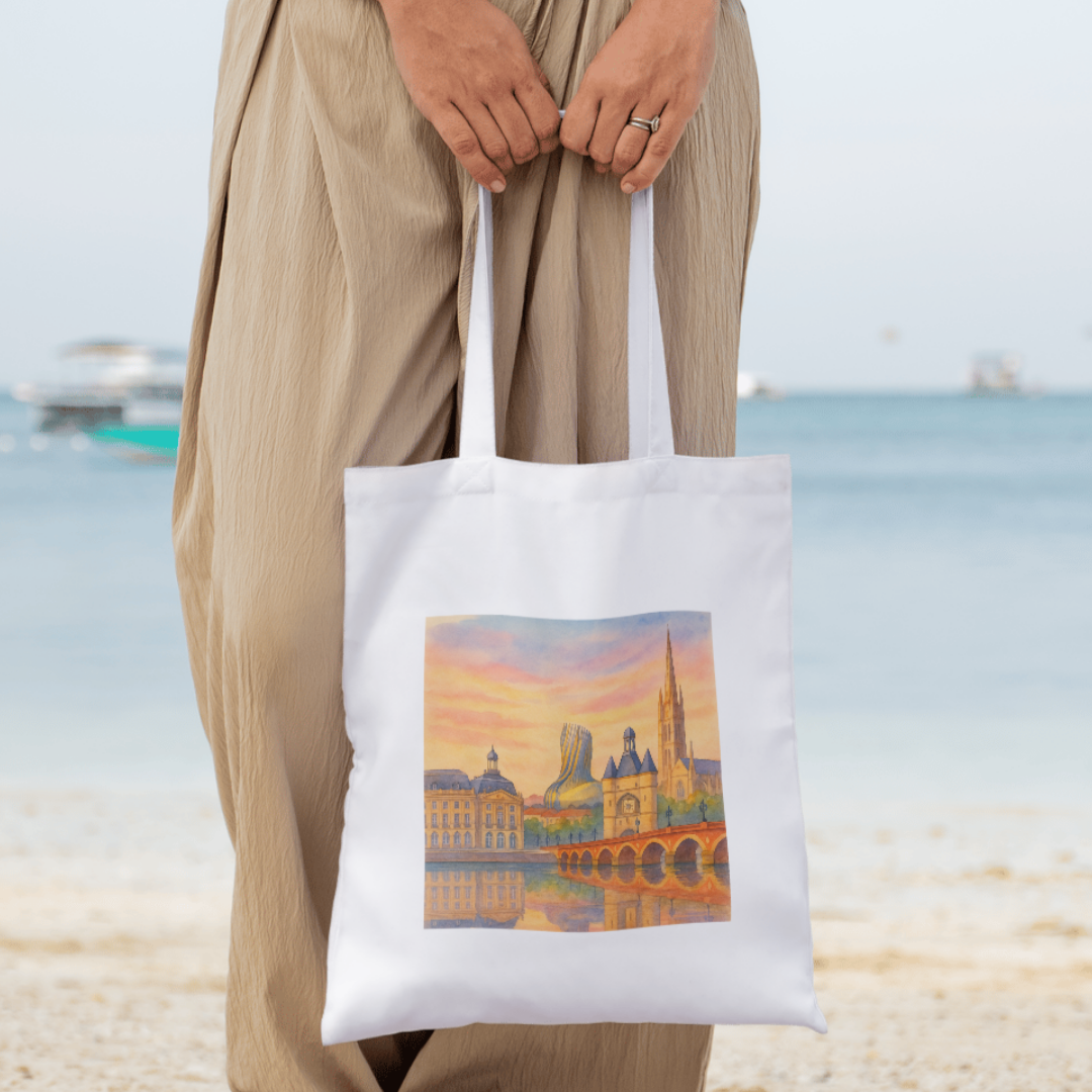 Person holding a tote bag with a Bodeaux scenic design on a beach